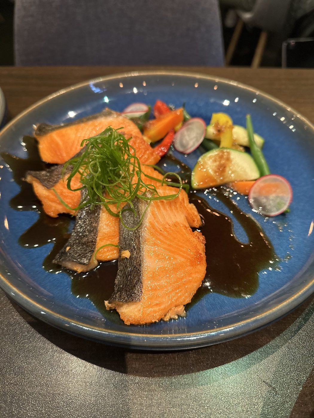 Fuga lightly grilled salmon on a dark plate with vegetables and sauce